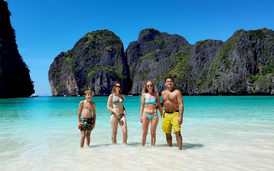 Four people standing in the shallows in front of limestone cliffs