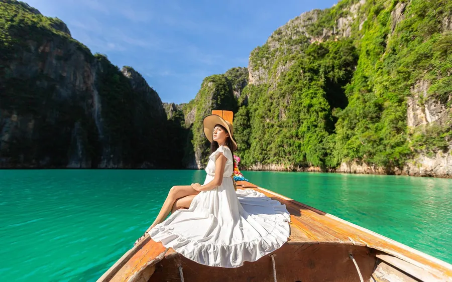 The bow of a wooden longtail boat on green water below limestone cliffs