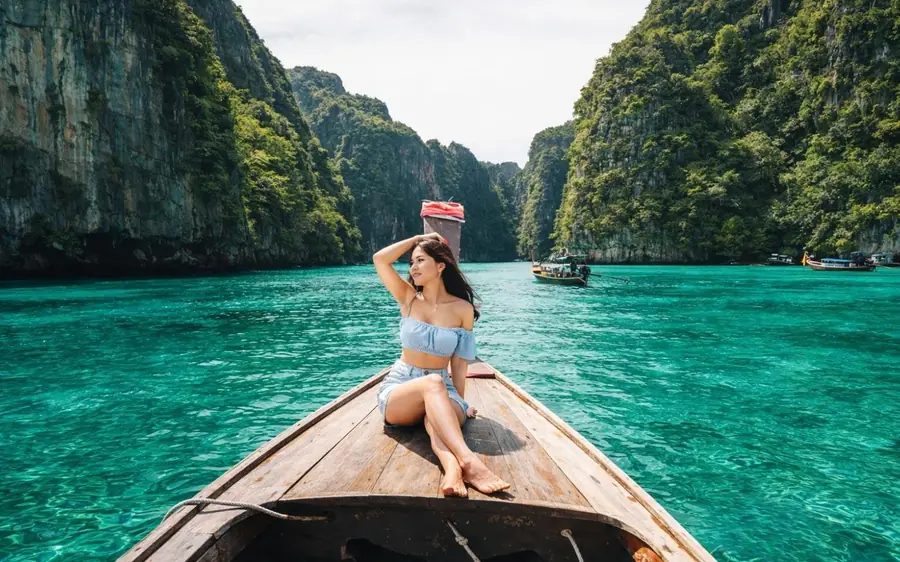 A wooden longtail boat on turquoise water between two limestone walls