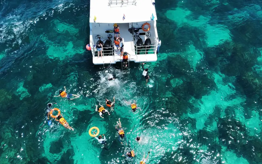 Swimmers with floats in the water beside a moored boat, seen from above