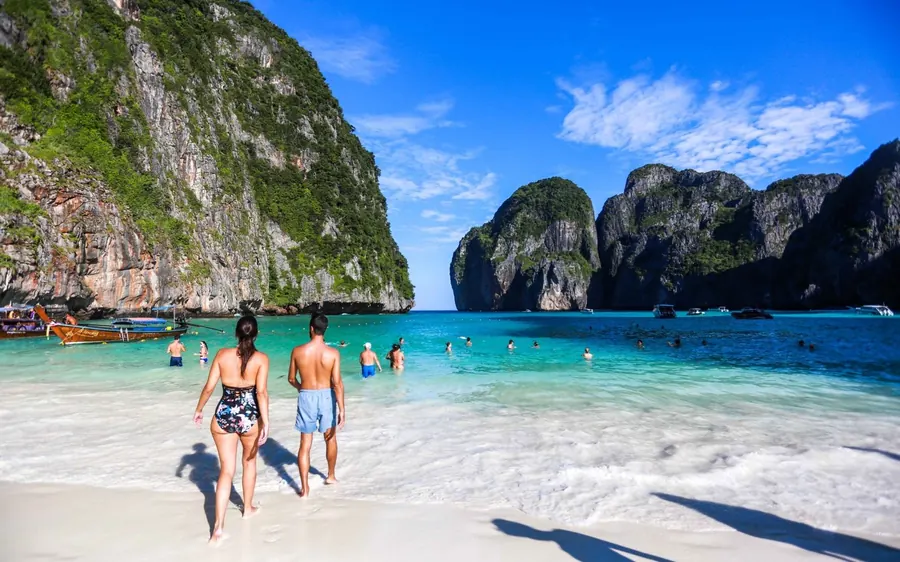 People walking along a white sand beach below steep limestone cliffs