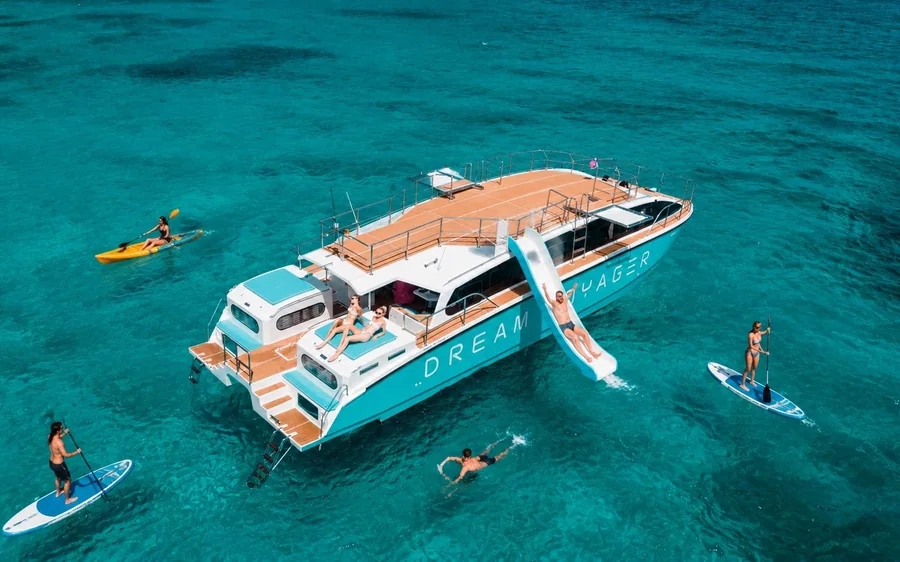 A speed catamaran at anchor with paddleboarders alongside it