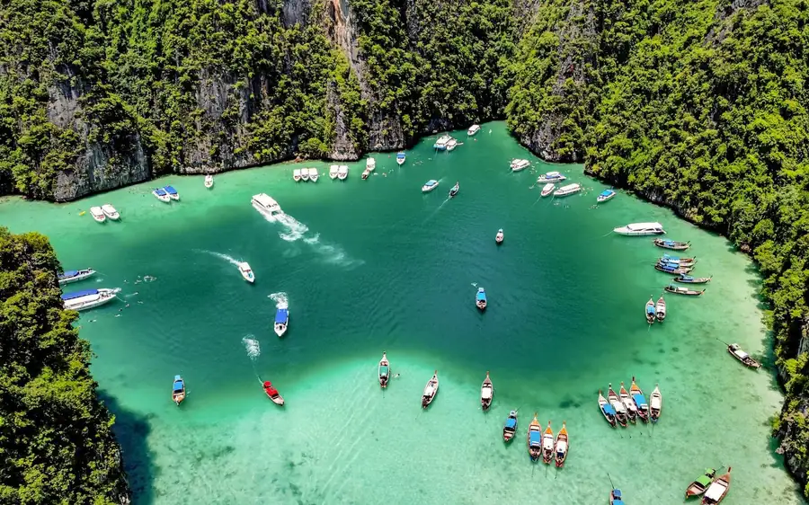 Longtail and speed boats moored in a green lagoon ringed by limestone cliffs