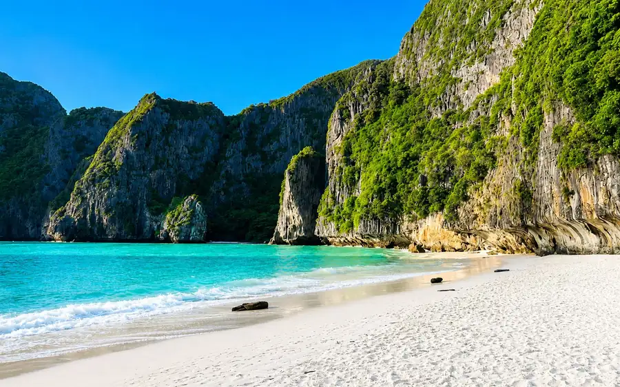 A white sand beach below limestone cliffs, with clear shallow water