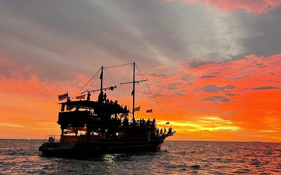 A tall wooden sailing boat silhouetted against an orange evening sky