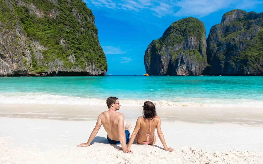 Two people sitting on the sand looking out across the bay