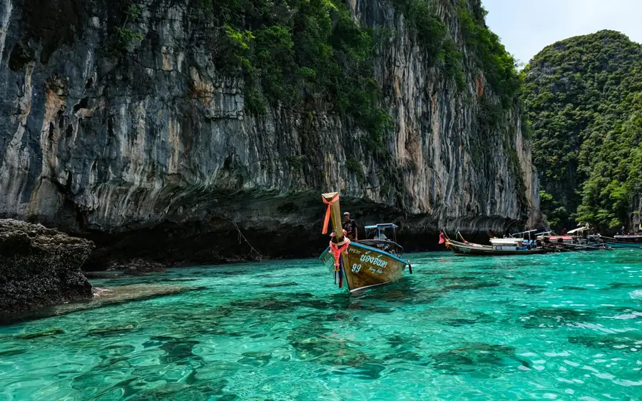 A longtail boat crossing turquoise water below a limestone headland