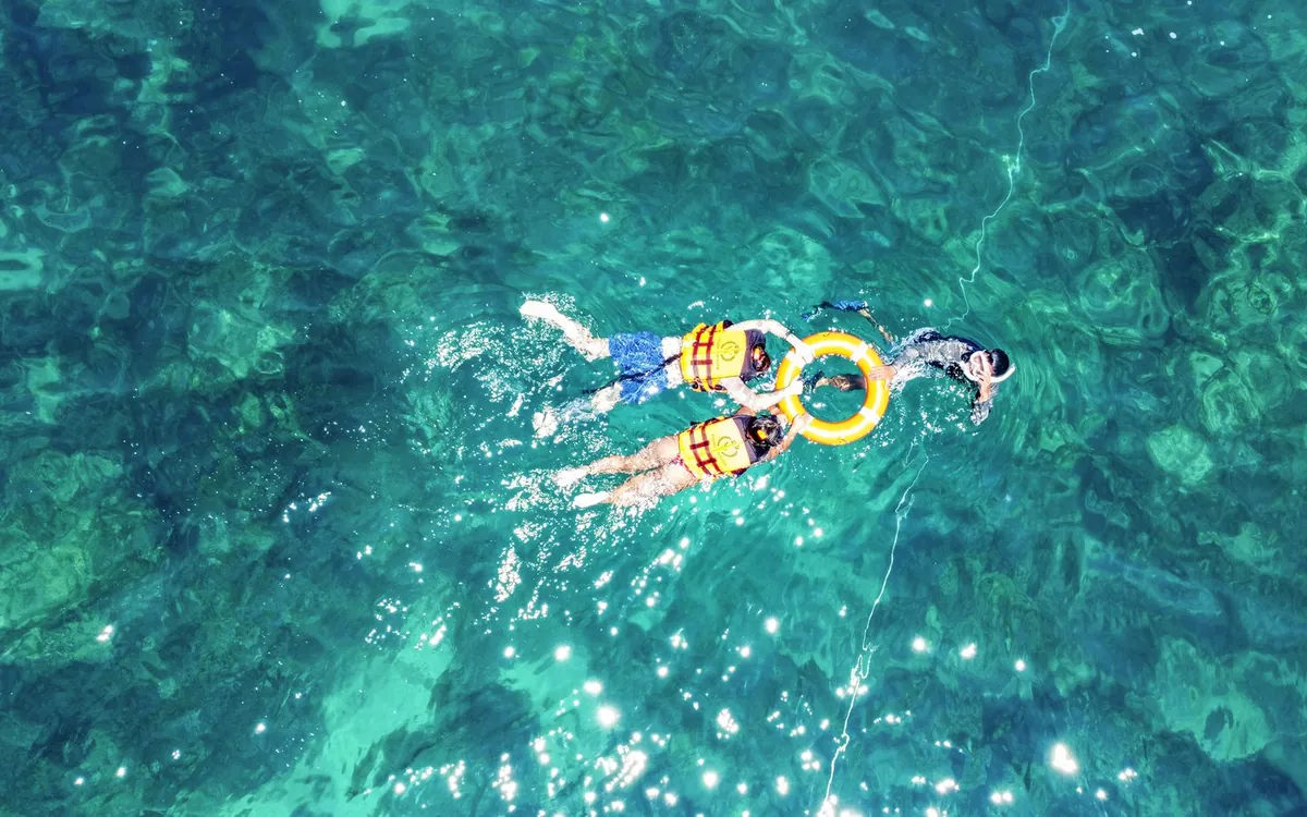 Two snorkellers in life jackets floating face down over a shallow reef, seen from above